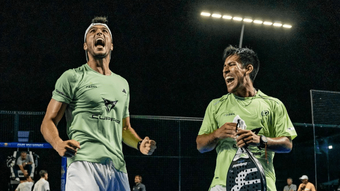 Zwei männliche Padelspieler, zukünftige Padel-Profis auf der Südamerika-Tournee von Premier Padel, feiern nachts in ihren grünen Trikots auf einem Freiluftplatz, ihre Gesichter strahlen vor Aufregung und Freude. Einer hält einen Padelschläger, während helle Lichter auf die Szene fallen.